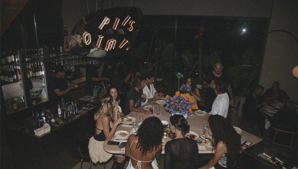 Candlelit interior at Optimist Bali — concrete bar, marble communal table, stone mosaic floor